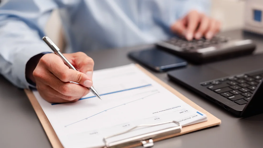 Budget manager reviewing a maintenance spending and performance trend report with a calculator and laptop
