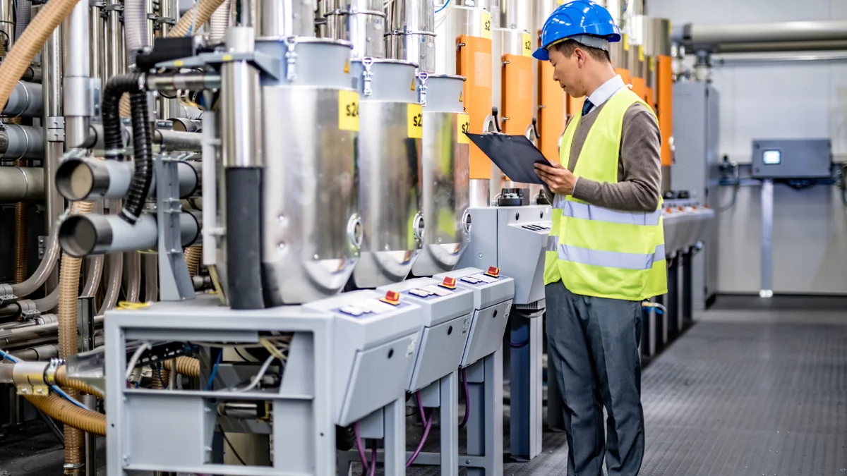 Technician with a clipboard checking equipment and control panels against a parts and service record