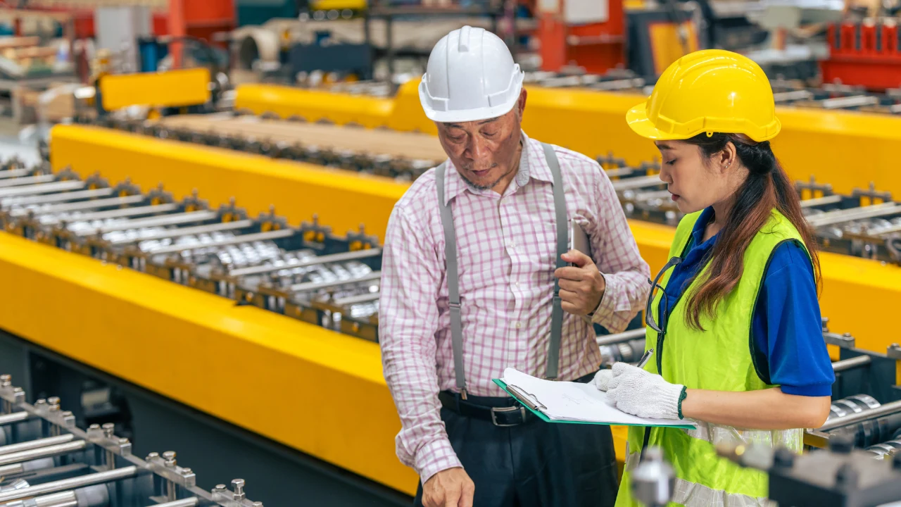 work-order-manager-alert-triggers Plant supervisor and maintenance technician reviewing a work order on a clipboard beside a roll forming line